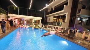 Una piscina con persone intorno, un edificio con balconi e una ringhiera.
