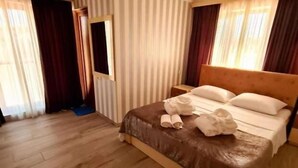 Una camera d'albergo con pavimento in legno, un letto con testiera marrone e tende a righe.