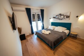 Ein Schlafzimmer mit einem Bett, einem runden Nachttisch, einem an der Wand montierten Fernseher und einem Fenster mit Vorhängen.