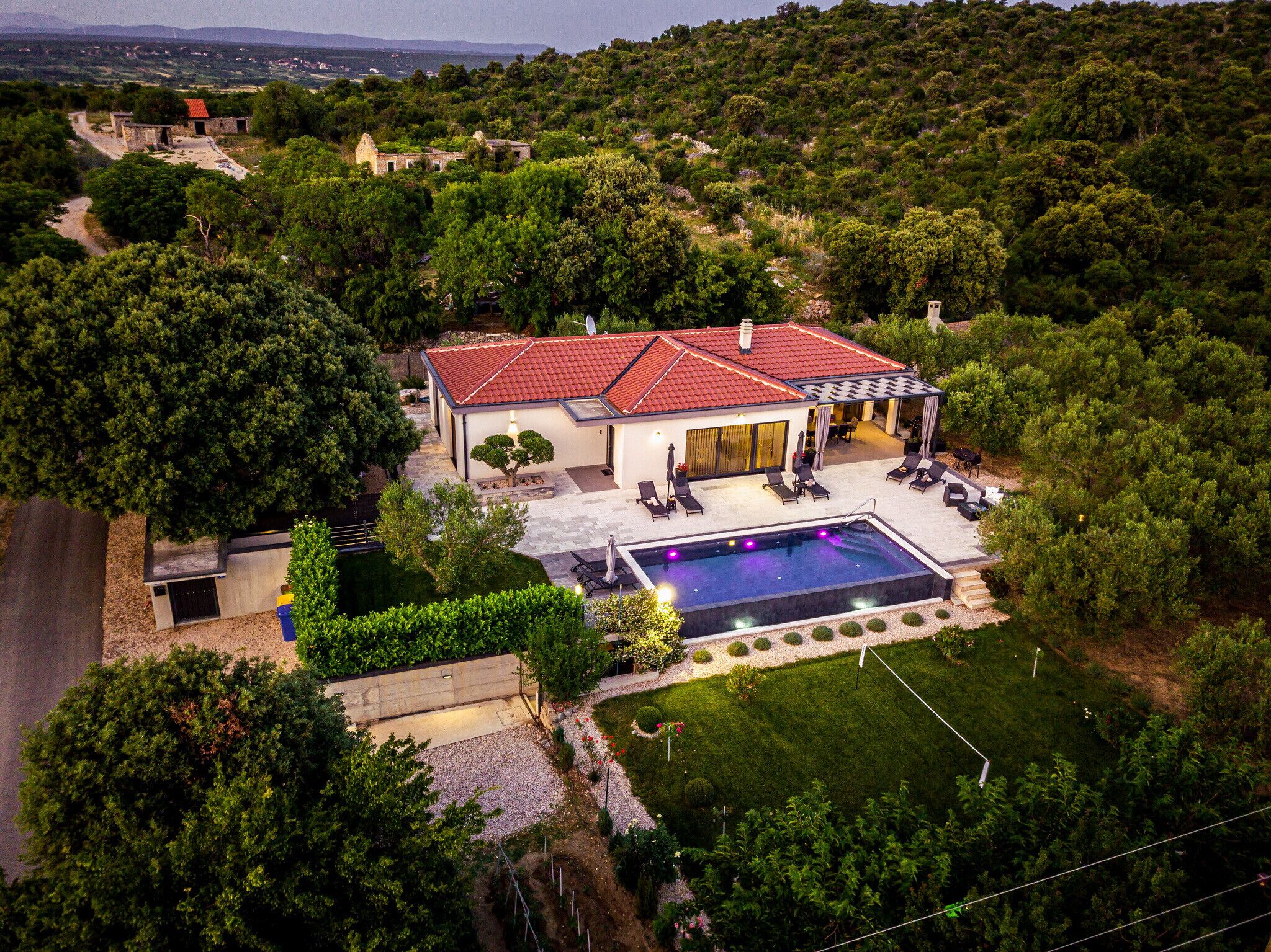 Et moderne hus med swimmingpool, omgivet af frodig vegetation og et kuperet landskab.