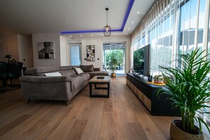 Ein modernes Wohnzimmer mit einer Couch, einem Couchtisch und einem Fernseher auf einem schwarzen Standfuß.