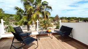 Un balcon avec deux chaises noires, une petite table sur laquelle se trouve un panier de fruits et une bouteille.