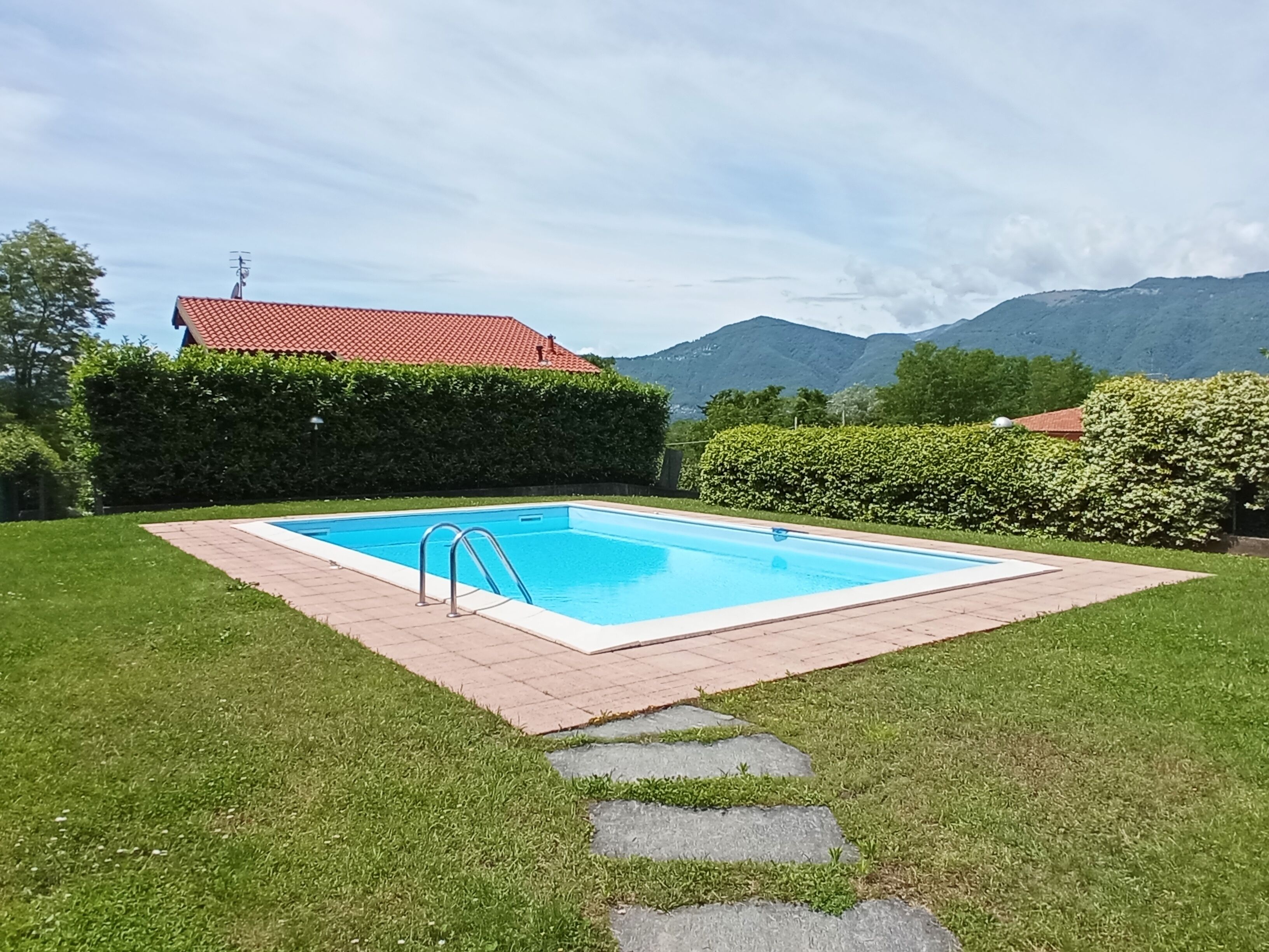 A rectangular swimming pool with a metal ladder, surrounded by a brick border and a stone pathway leading to it.