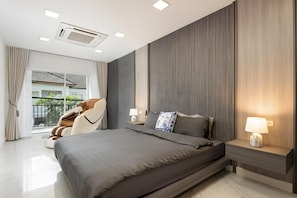 A modern bedroom with a large bed, a massage chair, a nightstand with a lamp, and a view of the outdoors through a large window. - Bangkok's Most Beautiful Modern  Villa (Bangkok)