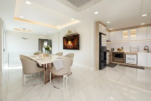 A modern kitchen with white cabinetry, a built-in oven, and a dining area with a marble floor and a white table. - Bangkok's Most Beautiful Modern  Villa (Bangkok)