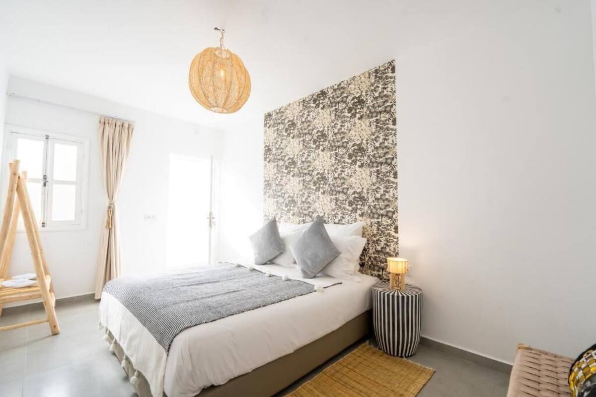 A bedroom with a bed, a bedside lamp, a wall tapestry, and a window with curtains.