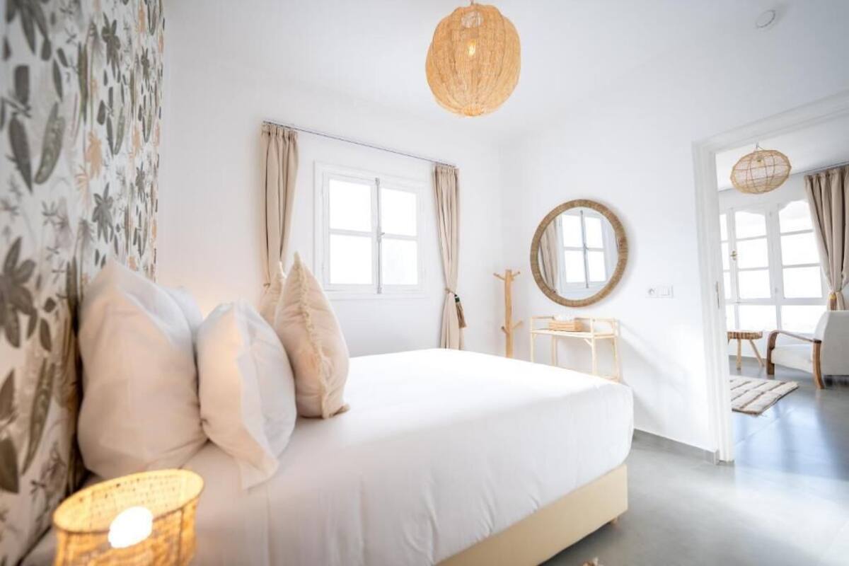 A bedroom with a bed, a round mirror, a window, and a door leading to another room.