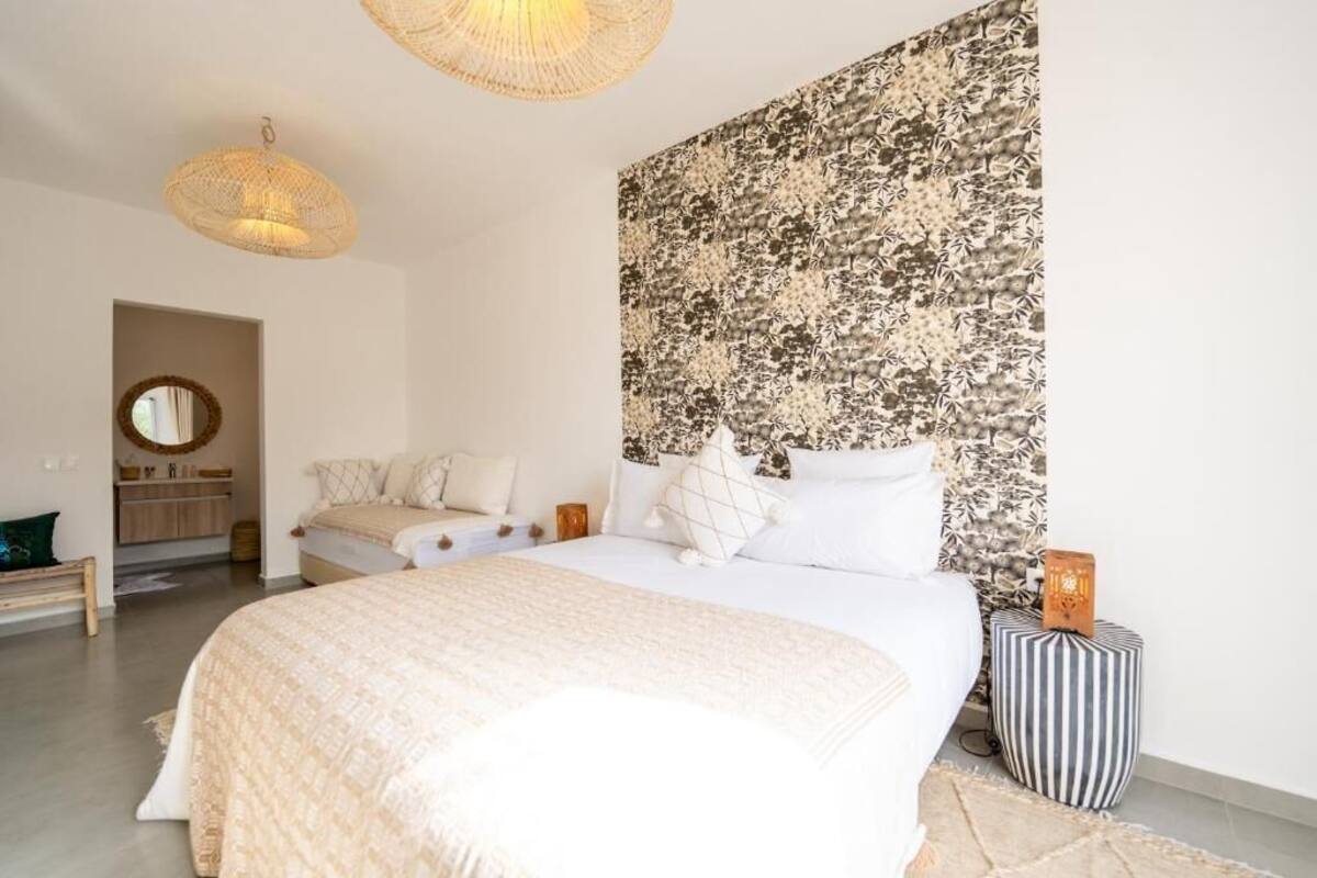 A bedroom with a large bed, a bedside table, a hanging light fixture, and a patterned wall.