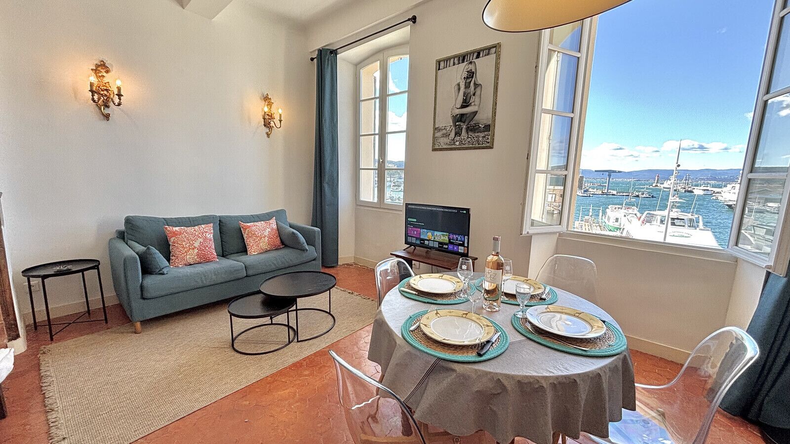 Een woonkamer met een bank, een salontafel, een eettafel gedekt voor vier personen en een televisie op een meubel.