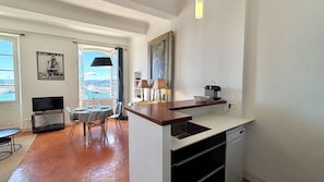 A compact living space with a dining area, kitchenette, and a large window offering a view of a marina.