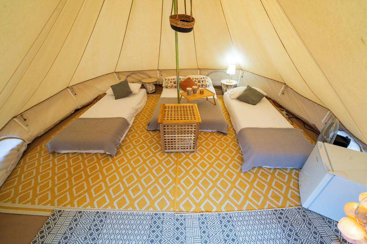 A tented accommodation with two beds, a small table with cups, and a hanging basket.