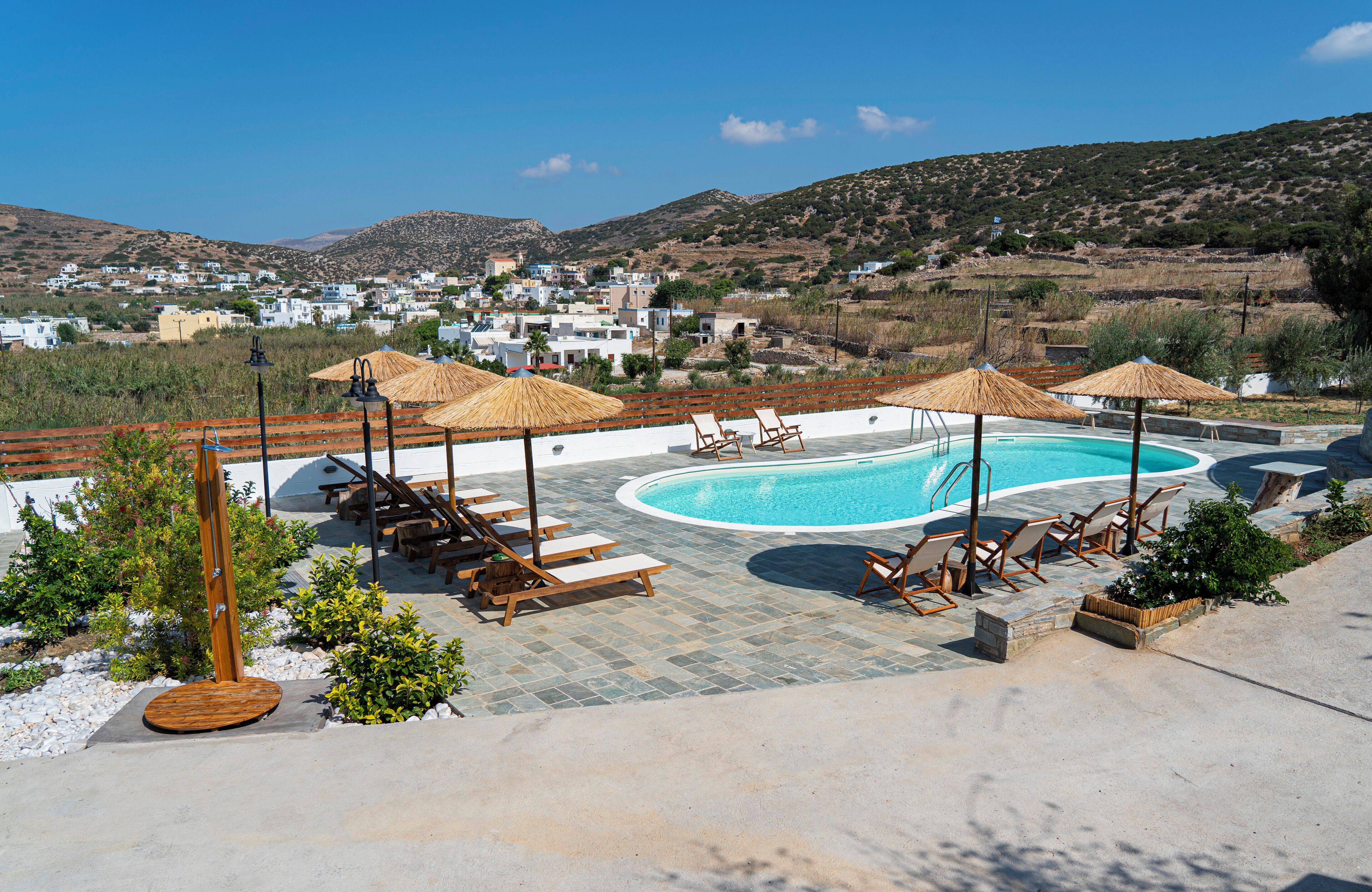 A pool area with lounge chairs and umbrellas, surrounded by a stone deck and a view of a hillside village.