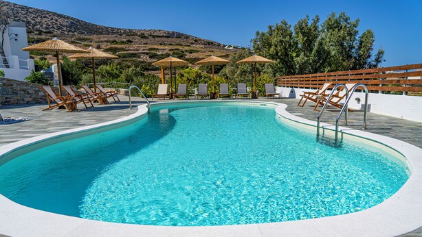 Uma piscina com espreguiçadeiras e guarda-sóis, cercada por muros de pedra e vegetação.