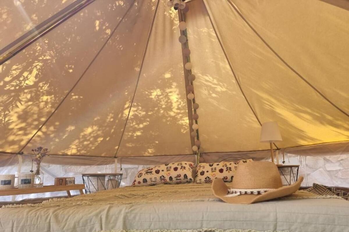 A tent with a bed, pillows with a pattern, a woven basket, and a hat.