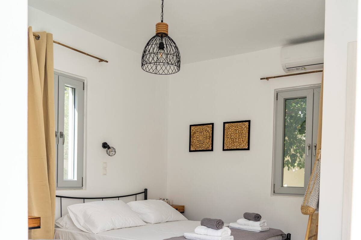 A modern bedroom with a bed, two bedside tables, a hanging light fixture, and a window.