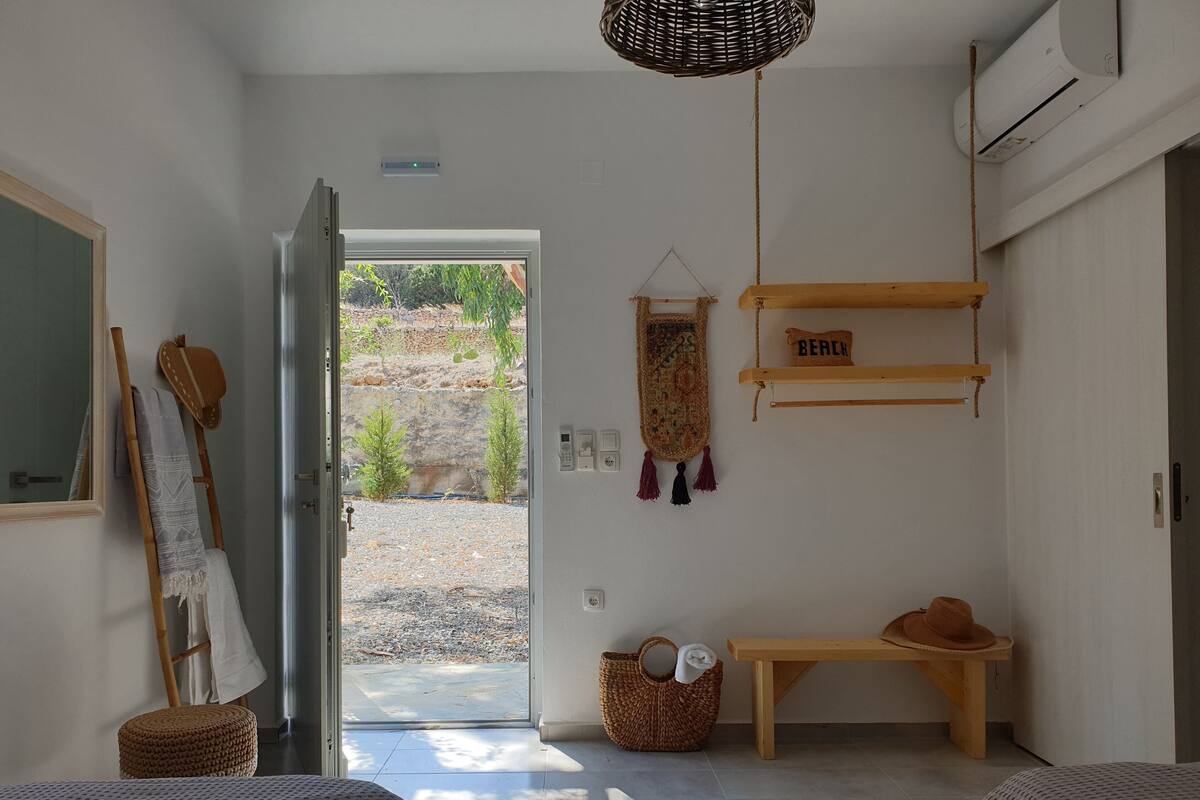 A room with a bed, a bench, a hanging basket, and a door leading outside.