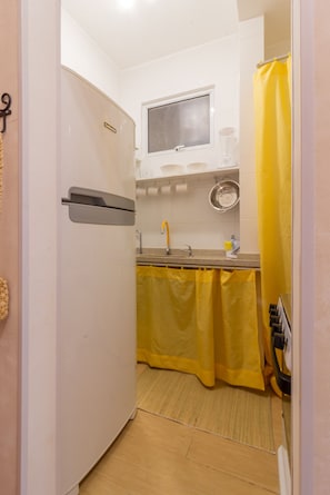 Cozinha compacta com geladeira, pia e cortinas amarelas.