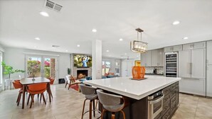 A modern kitchen with a large island, built-in appliances, and a dining area with a fireplace. - Remodeled Palm Desert Home by El Paseo: Mountain views, pool&spa, outdoor kitchen, sleeps 8 (Palm Desert)