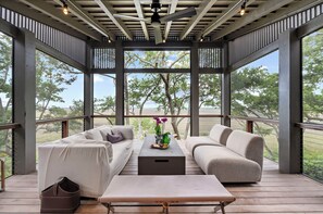 Ein überdachter Außenbereich mit einer Couch, einer Bank und einem Couchtisch, mit Blick auf Bäume und einen klaren Himmel.