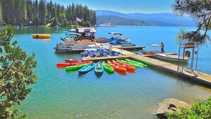 A lakeside dock with colorful kayaks and a small boat rental area. - Shaver Escape – Hot Tub Cabin Retreat with AC + Forest Views (Shaver Lake)