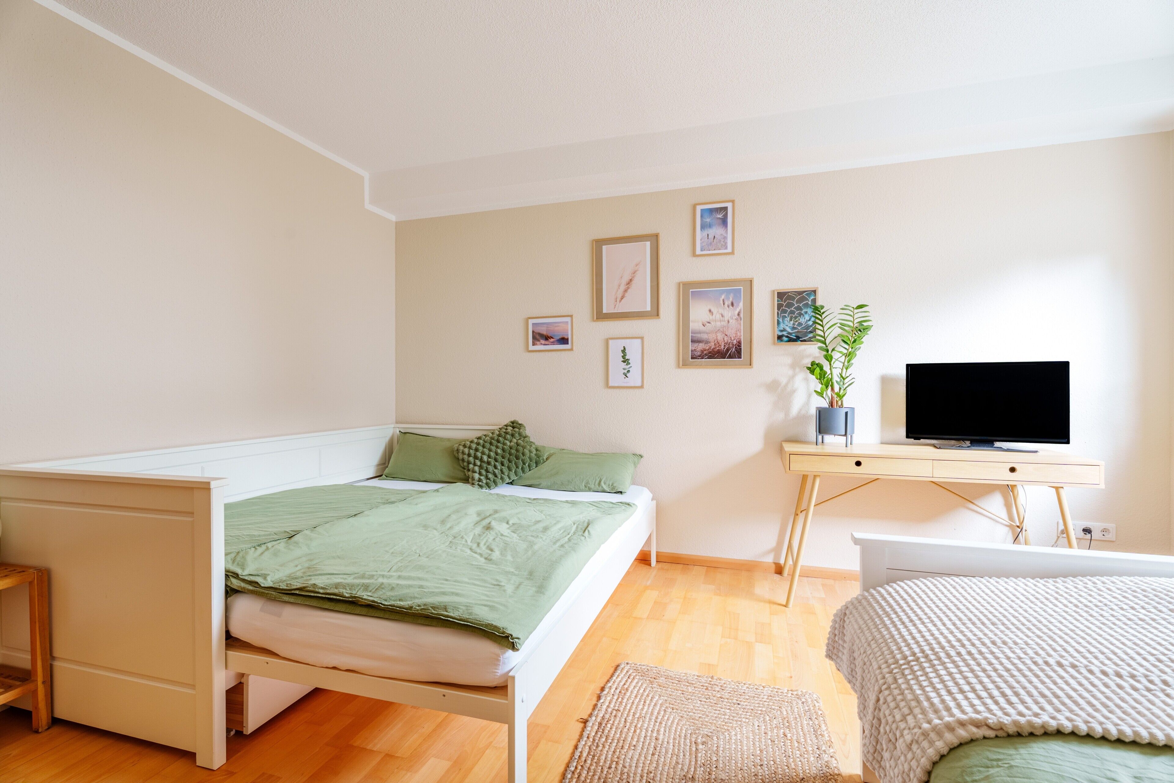Ein Schlafzimmer mit Bett, Schreibtisch, Fernseher und einer Wand mit gerahmten Bildern.