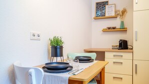 Un comedor con una mesa dispuesta para dos personas, una planta en maceta y una cafetera.