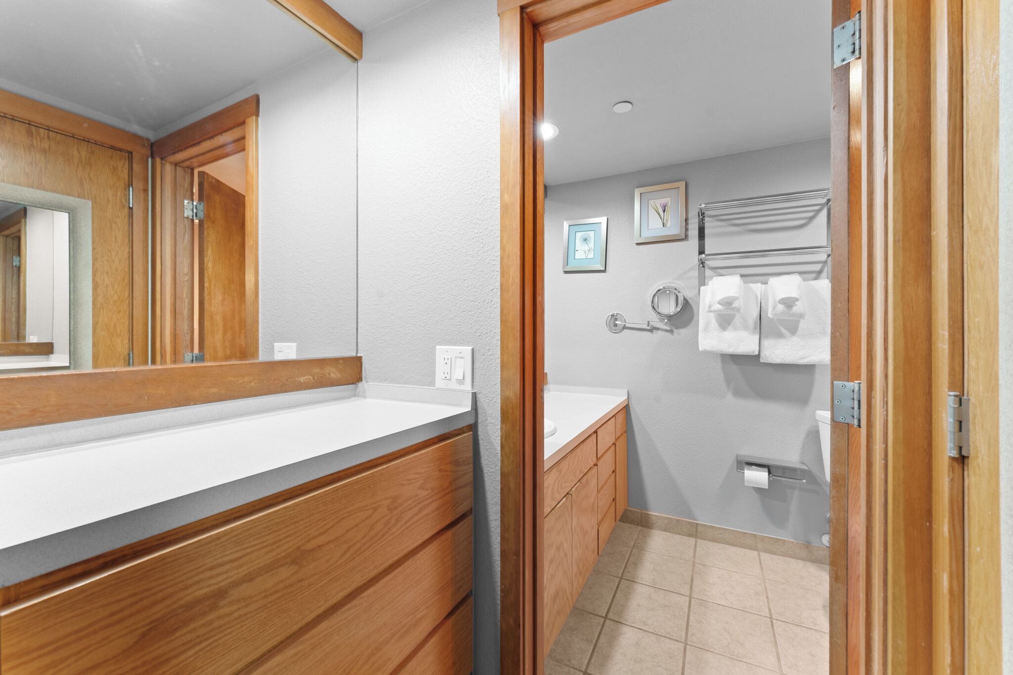 A modern bathroom with a wooden vanity, a large mirror, a toilet, and a towel rack.