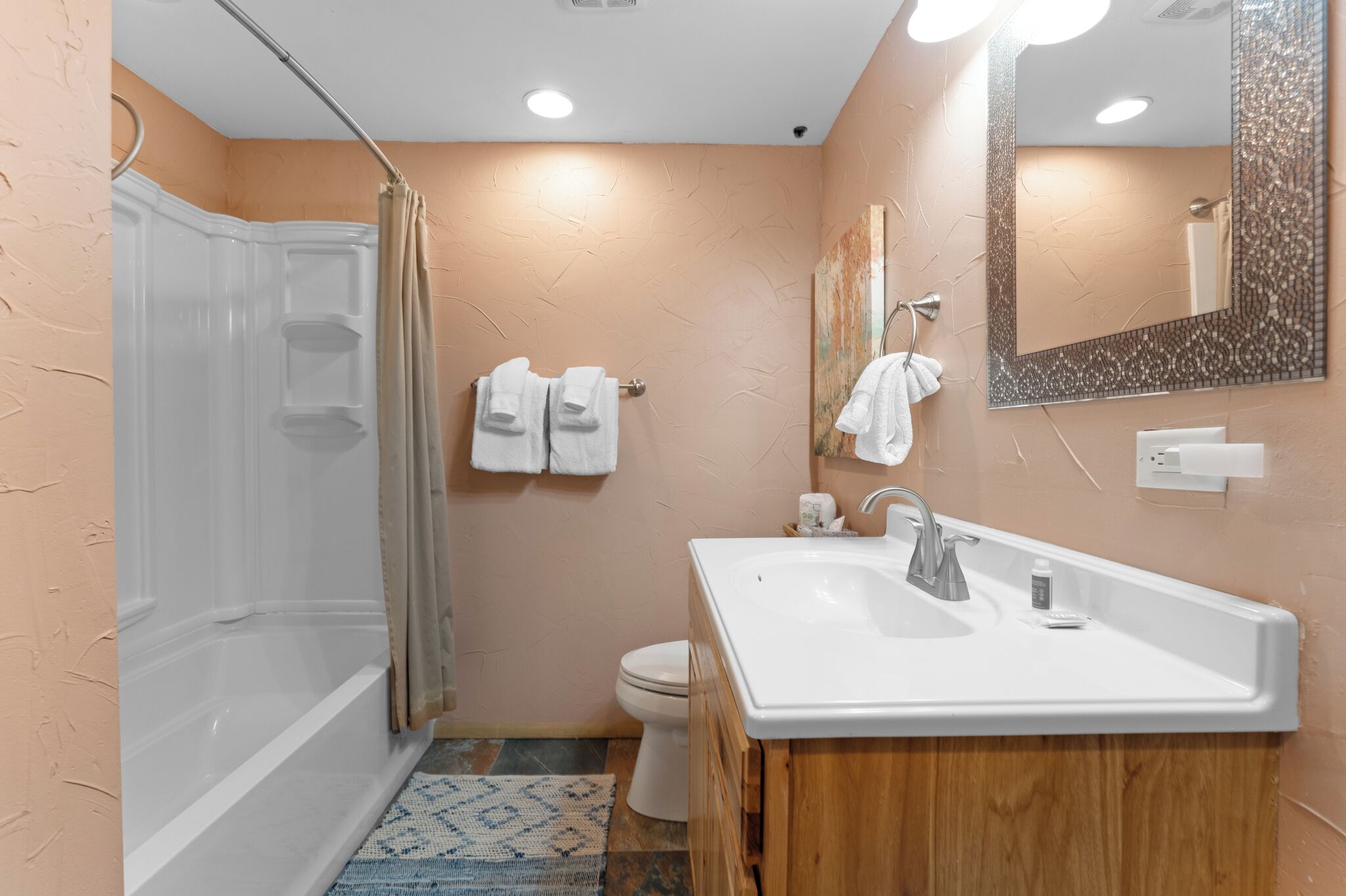 A bathroom with a shower, toilet, sink, and mirror.