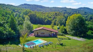 Un bâtiment en pierre doté d’une piscine et de chaises longues, entouré d’une végétation luxuriante et de collines.