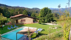 Un espace piscine avec des chaises longues, un petit bâtiment et une chaîne de montagnes en arrière-plan.