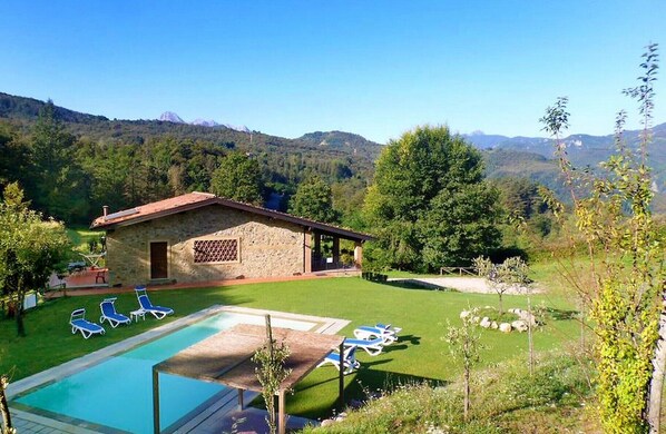Un espace piscine avec des chaises longues, un petit bâtiment et une chaîne de montagnes en arrière-plan.