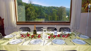 Une table à manger dressée pour six personnes, avec vue sur un paysage boisé par une grande fenêtre.