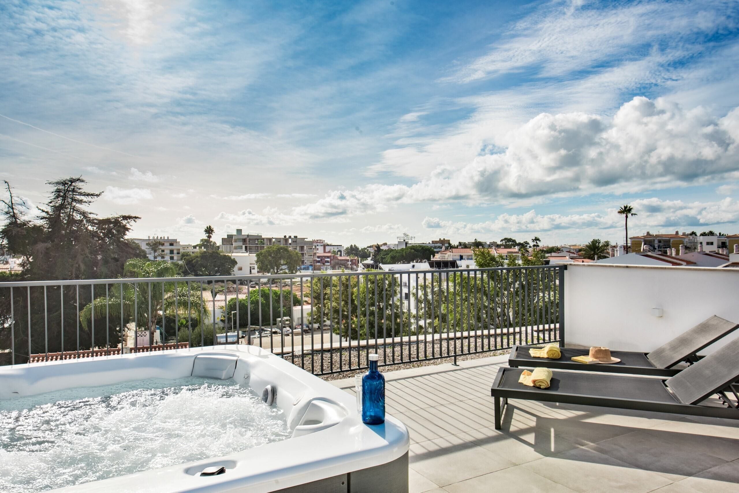 A rooftop terrace with a hot tub, lounge chairs, and a view of the cityscape.