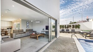 A modern living room with a sofa, coffee table, and a dining area. - Luxury 6BR Villa Margarida | Pool, Hot Tub & Walk to Albufeira Strip (Albufeira)