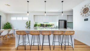 Una cocina moderna con una isla central, taburetes de bar, luces colgantes y un gran reloj de pared.