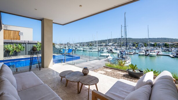 Un área de descanso al aire libre moderna con piscina, asientos y vistas a un puerto deportivo con barcos.