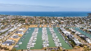 Un puerto deportivo con numerosas embarcaciones amarradas en una distribución ordenada, rodeado de edificios residenciales y una vista despejada del océano.