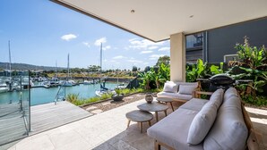 Un patio exterior moderno con un sofá, sillas y una mesa, con vistas a un puerto deportivo y barcos.