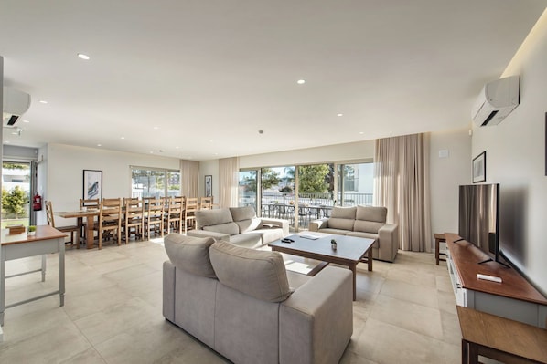 Un salon moderne comprenant un canapé, une table basse, un téléviseur et un coin repas avec des chaises et une table.
