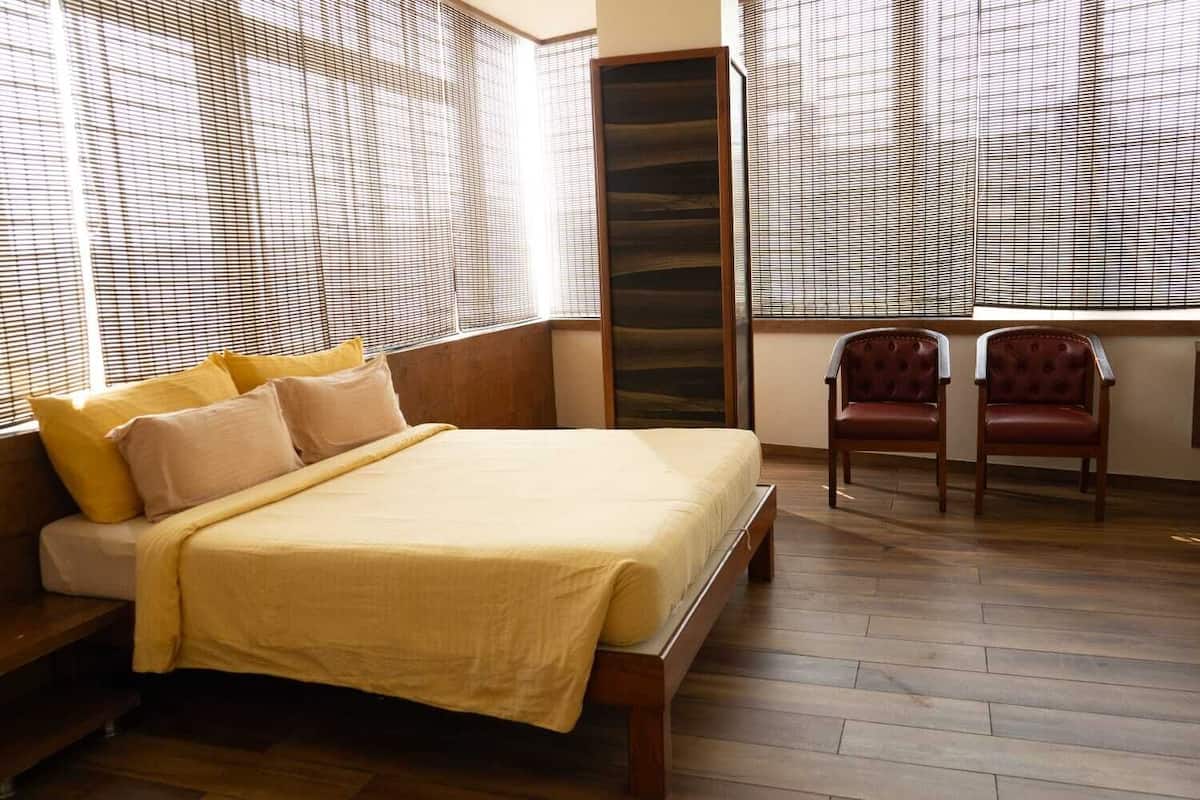 A bedroom with a bed, two chairs, and a large window with blinds.