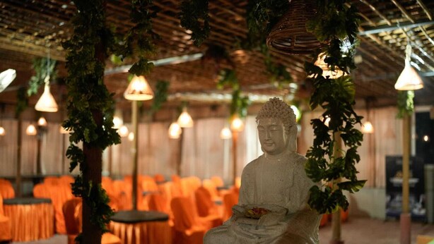 A Buddha statue in a room with orange chairs and hanging lights. - Hotel Grand Inn Jamkhandi (Jamkhandi)