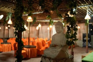 Una estatua de Buda en una habitación con sillas naranjas y luces colgantes.