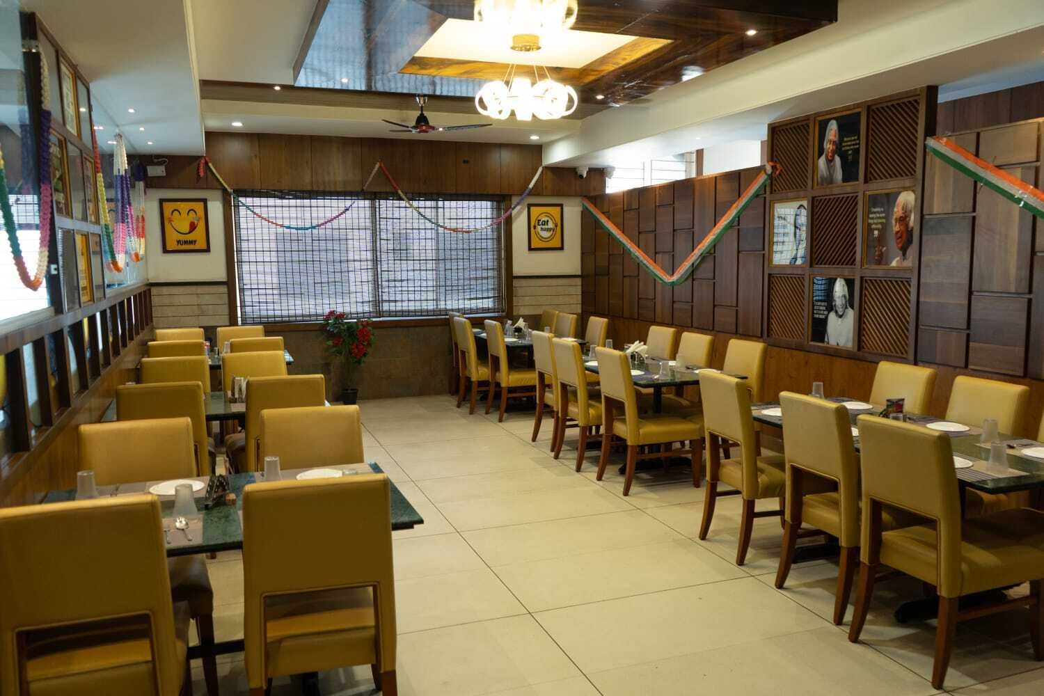 A restaurant with yellow chairs and tables, wooden paneling on the walls, and framed pictures.