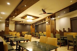 A restaurant with multiple dining tables and chairs, wooden accents, and ceiling fans.
