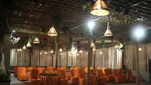 A room with rows of chairs covered in orange cloth, a ceiling with hanging lights, and a draped curtain backdrop. - Hotel Grand Inn Jamkhandi (Jamkhandi)