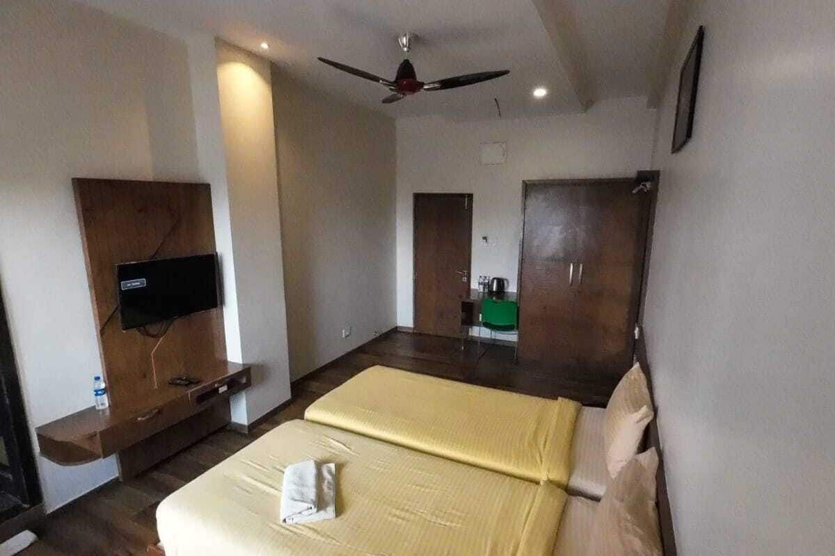 A hotel room with a large bed, a ceiling fan, wooden flooring, a flat-screen TV, and a wooden wardrobe.