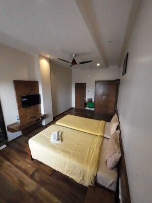 A hotel room with a large bed, a ceiling fan, wooden flooring, a flat-screen TV, and a wooden wardrobe.