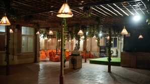 An indoor venue with a brick floor, orange chairs, and hanging lamps. - Hotel Grand Inn Jamkhandi (Jamkhandi)