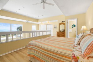 A bedroom with a large bed, a ceiling fan, a dresser, and a door leading to another room.