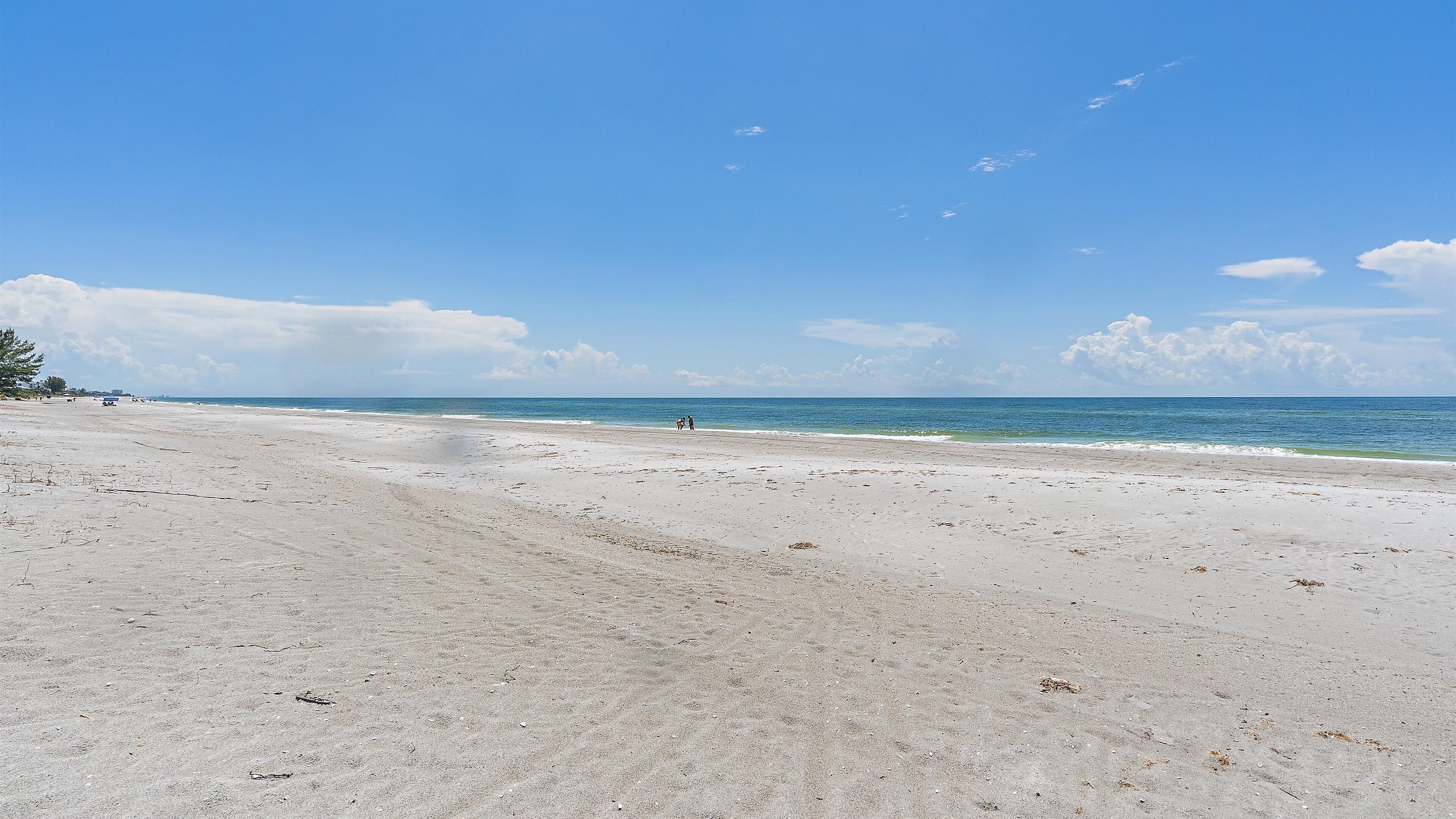 Een breed zandstrand met zachte golven, een heldere lucht en enkele verspreide wolken.